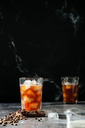 Iced coffee in a tall glass with poured cream, ice cubes and grains on an old rustic wooden table. Cold summer drink with pipes on black background with copy spaceの写真素材