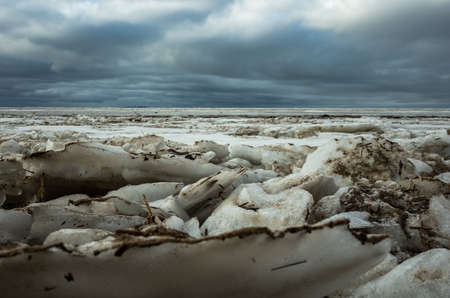 The landscape of the coastal strip of the Baltic Sea in early spring, the last snow background of the sea with grayish ice and cloudy sky.の写真素材