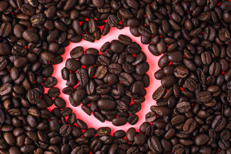 Coffee beans in the shape of a heart on a red background. Red heart made of coffee beans. Love of...