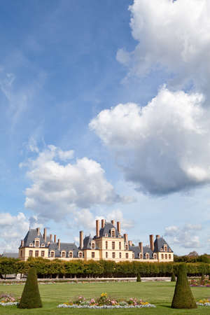 Medieval landmark royal hunting castle Fontainbleau near Paris in France and garden with flowers on the cloudy blue sky backgroundの写真素材