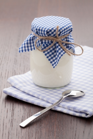 Homemade milk yogurt in glass pot and metal spoon served on linen napkin wooden tableの写真素材