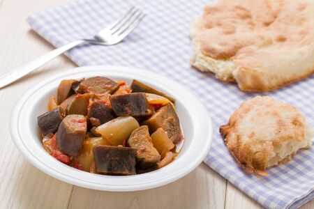 Cooked stewed eggplants in plate served with bread, fork on linen napkin and wooden tableの写真素材