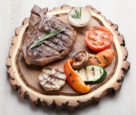 Portion of BBQ t-bone steak  served  on wooden board with  rosemary, mustard sauce  and grilled vegetables の写真素材