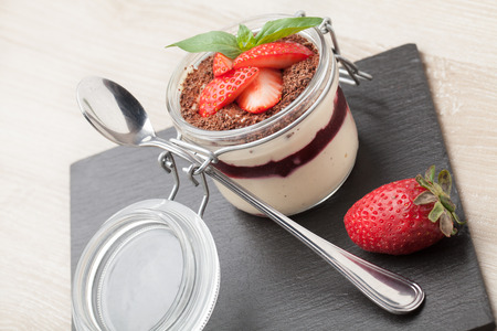 Delicious traditional italian cream dessert pannacotta with grated chocolate, strawberry, and basil served in jar with cocktail spoon on black stone backgroundの写真素材