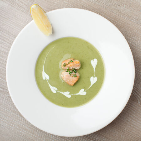 Green cabbage broccoli cream soup puree in white plate  served with  filleted salmon pieces , lemon and  themeの写真素材