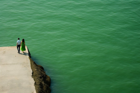 Captivating Encounter: A Man and Woman Stroll Alongside the Serene Green Seaの素材