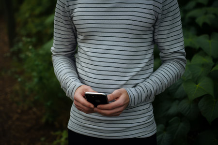 Stylish Man Posing with Smartphone in Trendy Striped Crew-neck Shirtの素材