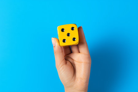 Exposing the Thrill: Captivating Blue Dice Held in Hand, Set Against a Vibrant Yellow Backdropの素材