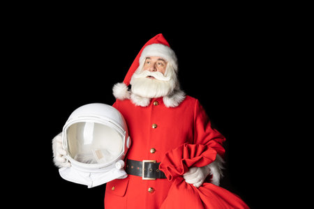 Santa Claus holds an astronaut's helmet in his hands and looks into the space. far. Close-up on a black background.の写真素材