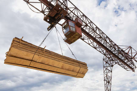 Cables of a cantilever gantry crane lift a stack of boards, a view from below against the background of clouds. Crane operation in production.の写真素材
