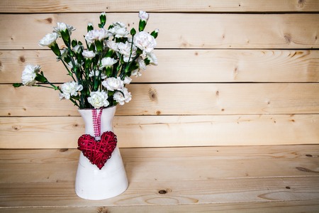 delicate bouquet of carnations in vintage vase with heart on wooden background. Valentine's Dayの写真素材