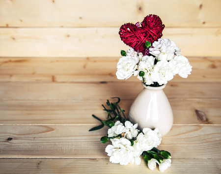 delicate bouquet of carnations in vintage vase with heart on wooden background. Valentine's Dayの写真素材
