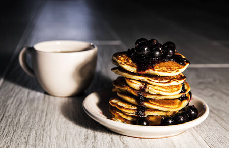 Picture of few pancakes with blackberries and cup of tea on wooden background