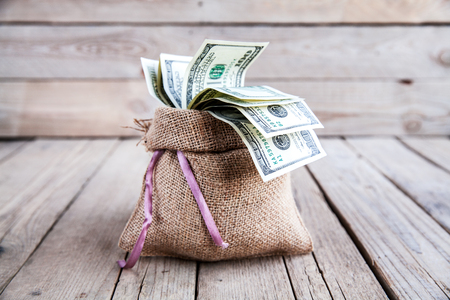 money in burlap sack on wooden backgroundの写真素材