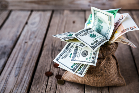 money in sackcloth and coins scattered on a wooden backgroundの写真素材