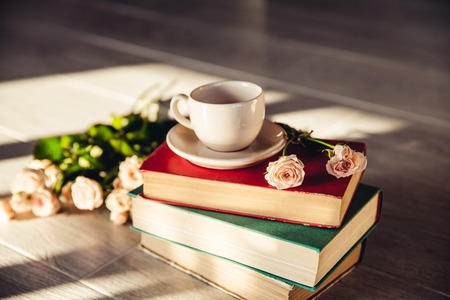 Beautiful bouquet of roses in the sun on the books with a cupの写真素材