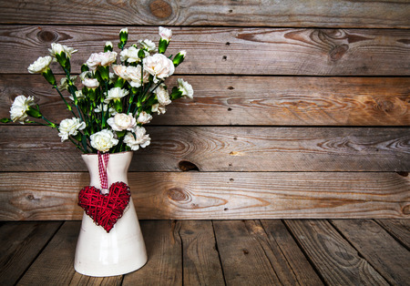 delicate bouquet of carnations in vintage vase with heart on wooden background. Valentine's Dayの写真素材