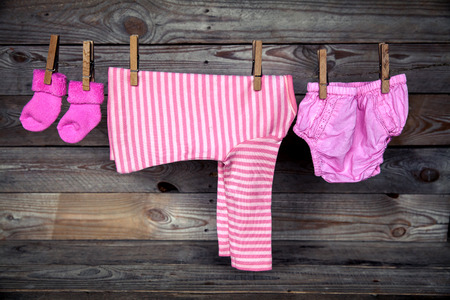 Baby clothes hanging on clothesline, on wooden backgroundの写真素材
