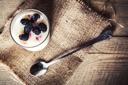 Serving of frozen creamy ice yoghurt  with whole fresh blueberries and wooden spoon with selective focus. Healthy sweet dessert with organic berries.の写真素材