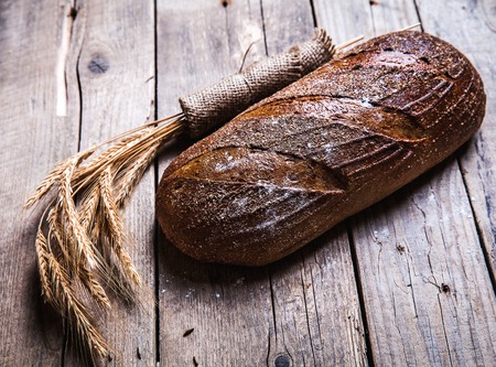 Rustic bread and wheat on an old vintage planked wood table. Dark moody background with free text space.の写真素材
