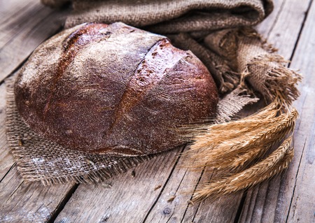 Rustic bread and wheat on an old vintage planked wood table. Dark moody background with free text space.の写真素材