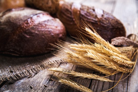 Rustic bread and wheat on an old vintage planked wood table. Dark moody background with free text...
