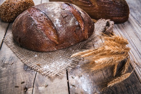 Rustic bread and wheat on an old vintage planked wood table. Dark moody background with free text space.の写真素材