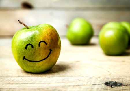 fresh green apples in plate on wooden background. with a smile on appleの写真素材