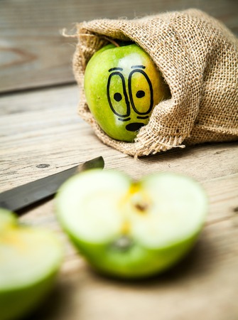 Knife slice apple on wooden background. Apple with painted face in shockの写真素材