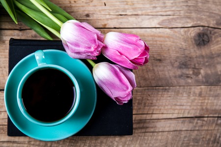 Cup of hot coffee on book with flowers on table on dark backgroundの写真素材