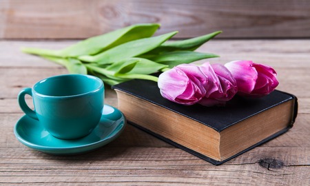 Cup of hot coffee on book with flowers on tableの写真素材
