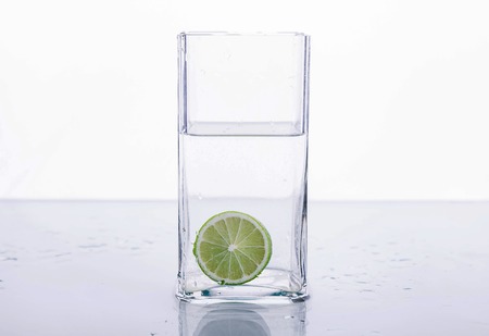 Lime splashing into glass of water on white backgroundの写真素材