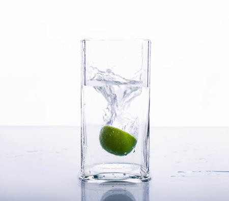 Lime splashing into glass of water on white backgroundの写真素材