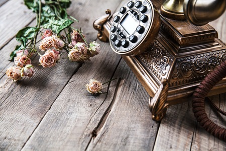 Old vintage black rotary phone and a bouquet of roses on wooden background