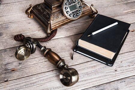 Vintage rotary telephone and old phone book on table near wallの写真素材
