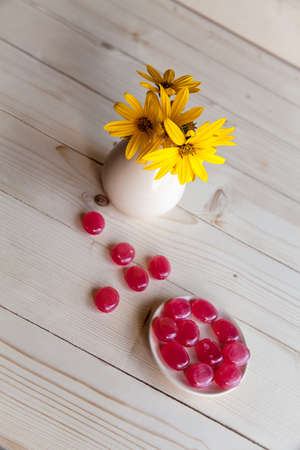 yellow flowers in a vintage vase with red candies on a wooden backgroundの写真素材