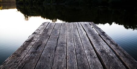 Beautiful glowing orange sunset over a rustic timber plank jetty reflected in the mirror calm waters of the lake below, a background of natural beauty and serenityの写真素材