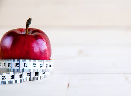 Diet concept with red apple and blue measuring tape on wooden table