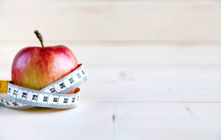 Diet concept with red apple and blue measuring tape on wooden tableの写真素材