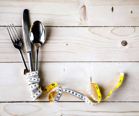 Empty plate with measure tape, knife and fork. Diet food on wooden tableの写真素材