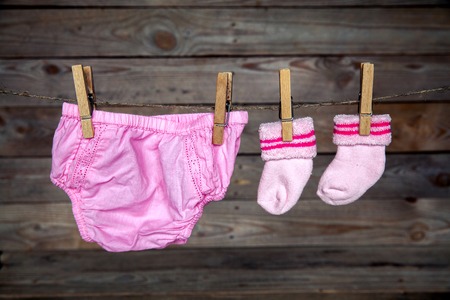 Baby clothes hanging on clothesline, on wooden backgroundの写真素材