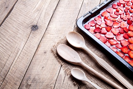 fruit. sliced Strawberry with wooden spoons baking on a dark metal plate in oven. wood backgroundの写真素材