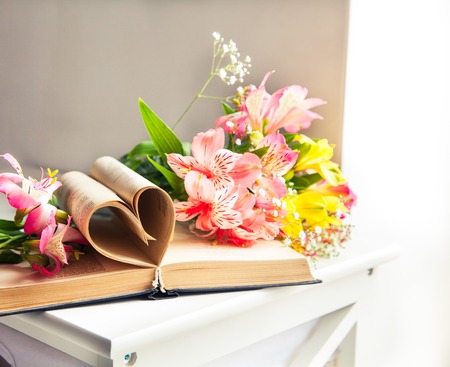 Alstroemeria flowers with book in vase on table on light backgroundの写真素材