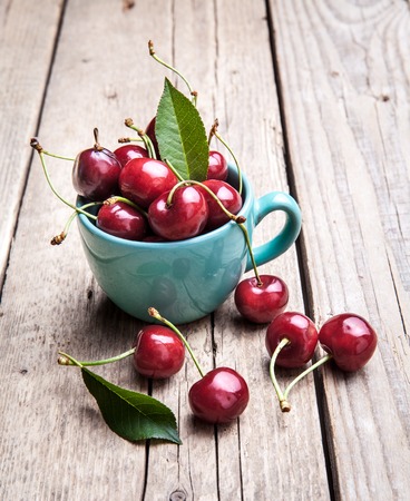 Cherries in the beautiful turquoise cup on wooden table, macro background, fruits, berriesの写真素材