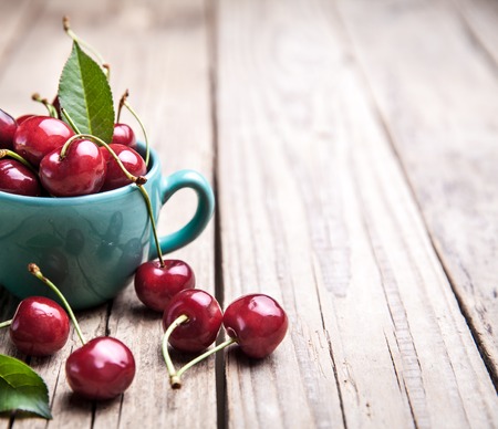 Cherries in the beautiful turquoise cup on wooden table, macro background, fruits, berriesの写真素材