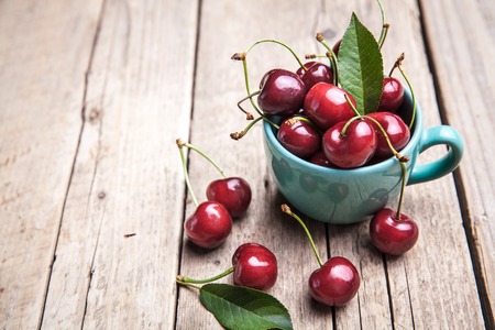 Cherries in the beautiful turquoise cup on wooden table, macro background, fruits, berriesの写真素材