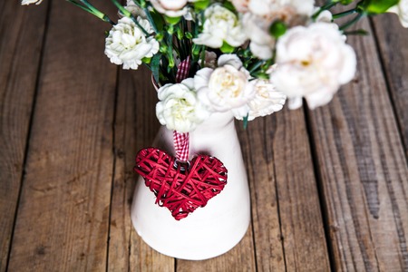 delicate bouquet of carnations in vintage vase with heart on wooden background. Valentine's Dayの写真素材