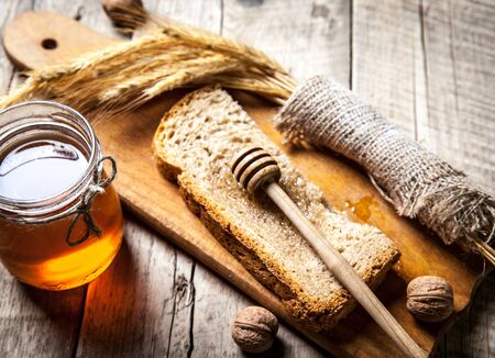 Honey in a jar, slice of bread, wheat and milk on an old vintage planked wood table from above. Rural or rustic style breakfast concept. Background layout with free text space.の写真素材