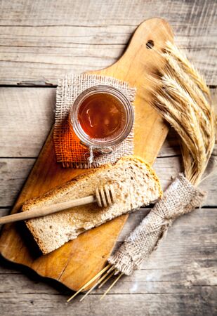 Honey in a jar, slice of bread, wheat and milk on an old vintage planked wood table from above. Rural or rustic style breakfast concept. Background layout with free text space.の写真素材