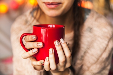 Woman's hand holding a red cup of coffee. With a beautiful winter manicure. Drink, fashion, morningの写真素材